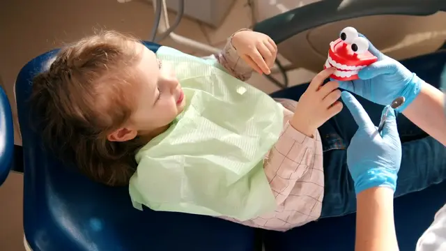 Niña en el sillón del dentista jugando con unos dientes de juguete